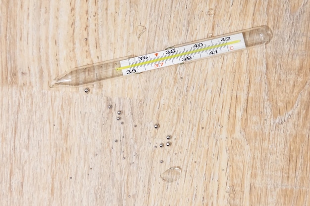 Termômetro médico aleatoriamente quebrado para medir fragmentos de vidro de temperatura corporal de uma pessoa e gotas de mercúrio perigoso no chão