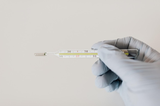 termómetro de mercurio con la mano del médico que usa guante de goma sobre fondo blanco.