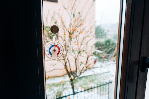 Termómetro redondo en la ventana. 5 grados centígrados. La nieve fuera de la ventana.