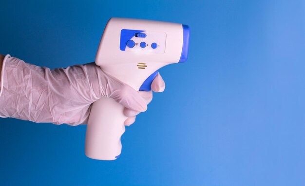 Termômetro sem contato na mão de um homem em uma luva médica em um fundo azul claro