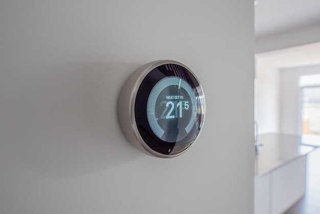 Termostato digital programable moderno redondo en una pared blanca limpia en modo de calefacción