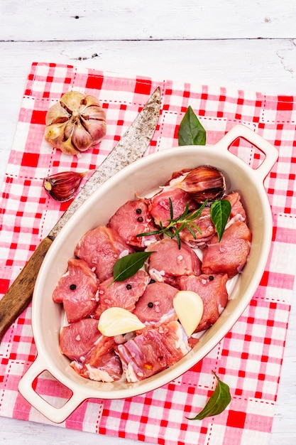 Ternera cruda cortada en trozos con verduras y otros ingredientes lista para cocinar. Mesa rústica de madera blanca, concepto culinario orgánico, espacio de copia