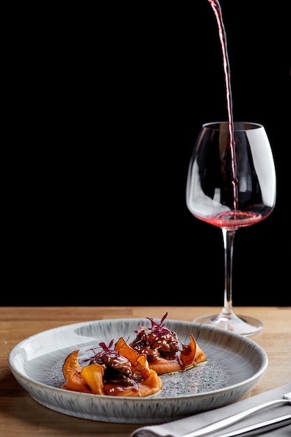 Ternera con salsa y boniato en una mesa de restaurante con una copa de vino cerca de la cena en el restaurante con fondo oscuro