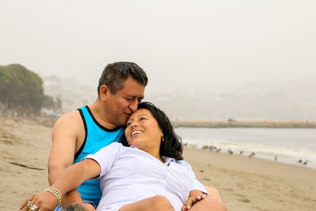 Terno casal étnico mais velho e apaixonado, sentado na areia em uma praia