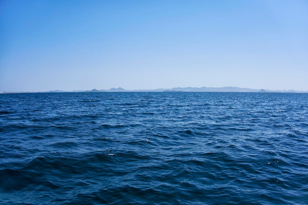 Terra firme e montanhas vistas à distância de um mar calmo em um dia ensolarado com céu claro e céu azul