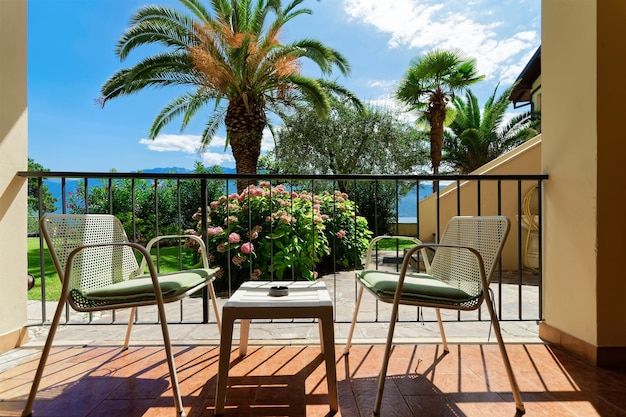 Terraço com mesa e cadeiras com vista para palmeiras tropicais no Lago Garda em Gargnano na Itália. Varanda no conceito de café ou restaurante. Vista da varanda em apartamento residencial moderno ou hotel.