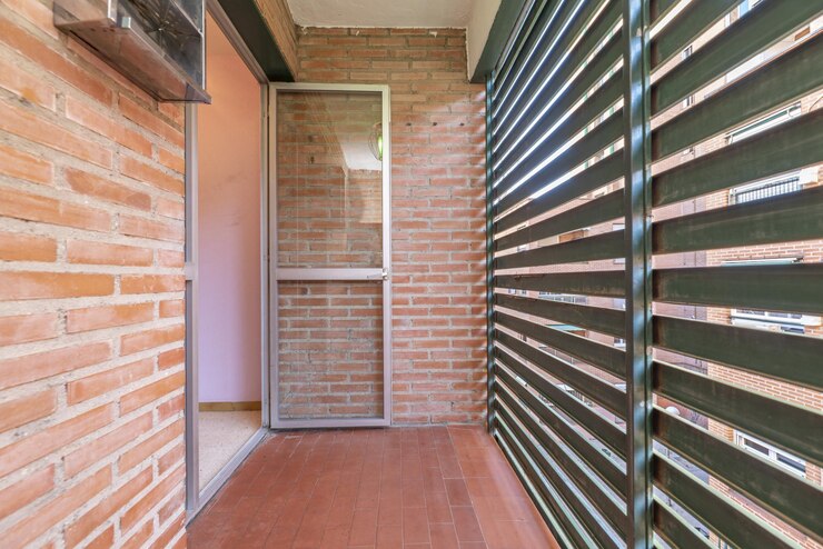 Foto terraço de estendal com parede de malha metálica de uma casa com piso de tijolos do mesmo material e acesso com porta de alumínio