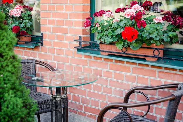 Terraço de verão em um café com parede de tijolos e flores frescas, mesa e poltrona