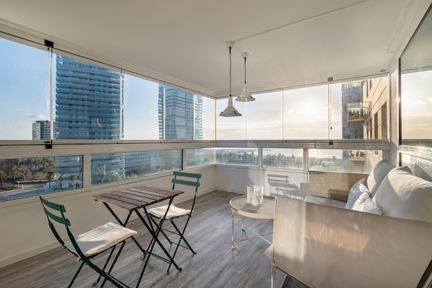 Terraço ensolarado com sofá, mesa e cadeiras. Bela vista panorâmica do bairro marítimo de Barcelona com edifícios modernos.