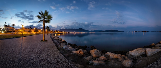 Terraplén con un camino y palmeras iluminadas por linternas temprano en la mañana. Panorama. Fethiye, Turquía