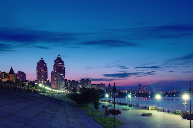 Terraplén de la ciudad europea moderna con iluminación nocturna y cielo colorido. Tarde en el río Dnieper en Obolon, Kiev