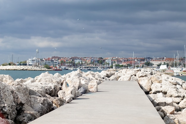 Terraplén de roca en el mar y estacionamiento del muelle para barcos. Cielo atronador y gaviotas.