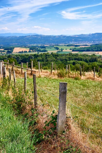 Foto terras agrícolas com uma cerca e um fundo de céu azul nublado paisagem de uma fazenda de agricultura sustentável com feno como grama e árvores em um ambiente verde com uma barreira de arame farpado na zona rural