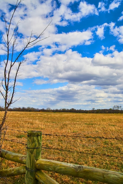 Terras agrícolas de primavera por cerca de madeira e arame farpado com nuvens fofas e céu azul em cima