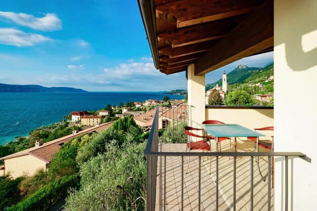 Terrasse mit Tisch und Stühlen mit Blick auf den Gardasee in Gargnano in Italien. Veranda im Café- oder Restaurantkonzept. Urlaub Sommerdesign. Balkonblick in modernen Wohnwohnungen oder Hotels.