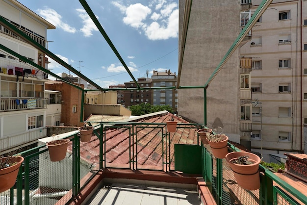 Terraza del ático con macetas de barro con celosía de metal verde y vistas de los tejados y otras casas