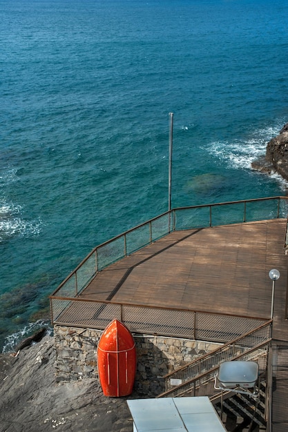 una terraza de playa hecha de tablas en la orilla con rocas del mar Mediterráneo un bote salvavidas rojo