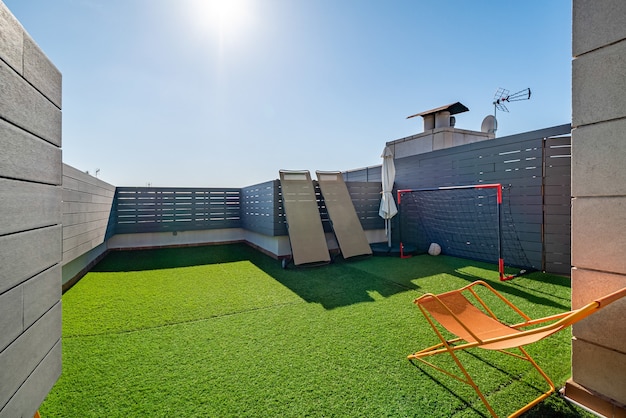 Terraza privada con hamacas, puertas de fútbol para niños y césped artificial en un día soleado con cielo azul