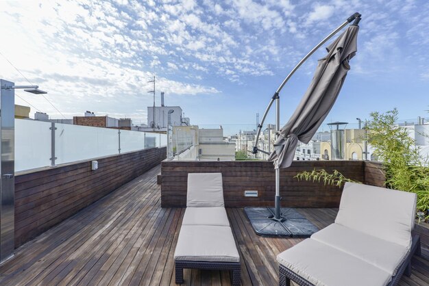 Foto terraza en el techo de un edificio con hamacas de ratán, tableros de madera de acacia, sombrilla plegada y mamparas de vidrio