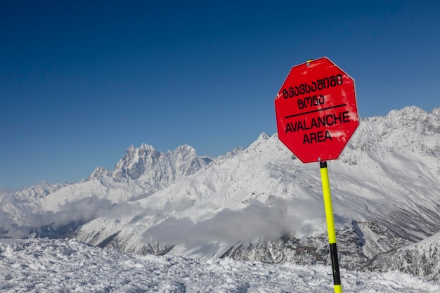 Terreno de avalanche perto de uma encosta de montanha A inscrição no sinal vermelho "Cuidado com avalanche"