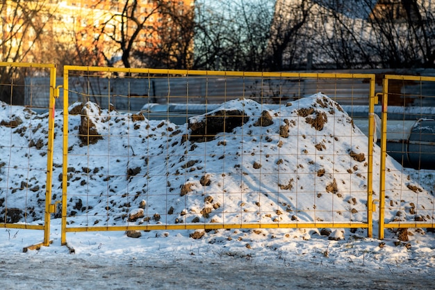 El terreno excavado en la nieve en invierno está vallado con una valla metálica con malla y cinta de barrera.