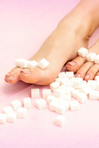 Terrones de azúcar en una fila sobre los pies femeninos sobre fondo rosa con espacio de copia, concepto de depilación.