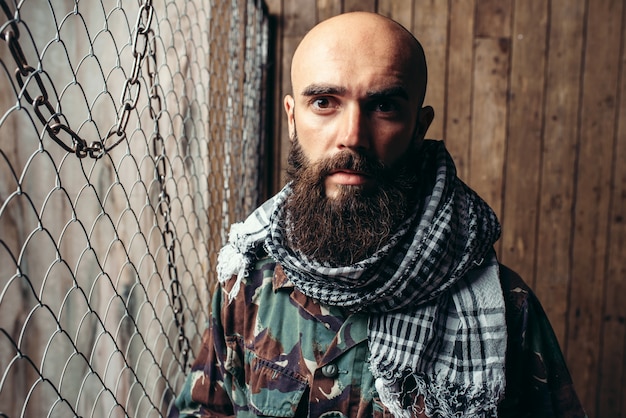 Terrorista barbudo em uniforme contra grade de metal