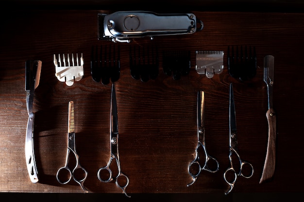 Foto tesoura, barbeador, aparador e bicos estão sobre uma mesa de madeira, um conjunto de equipamentos de barbeiro, ferramentas de cabeleireiro