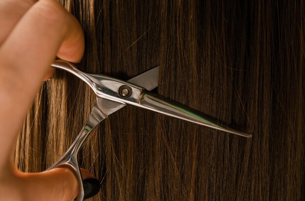 Foto tesoura e cabelo castanho fecham o plano de fundo da textura do cabelo da mulher estilista cortando cabeleireiro corta o cabelo com tesoura cabeleireiro de salão de cabeleireiro