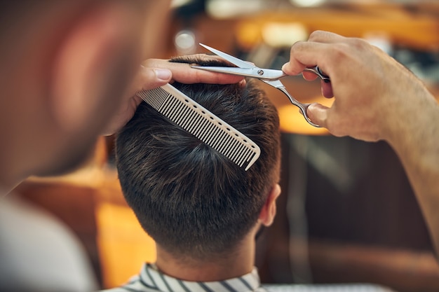 Foto tesouras e um pente de cabelo nas mãos de um barbeiro profissional trabalhando no corte de cabelo de seu cliente