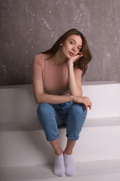 Test-Fotoshooting für ein junges, wunderschönes Model in Jeans-Shorts und rosa T-Shirt, das auf einer Treppe sitzt