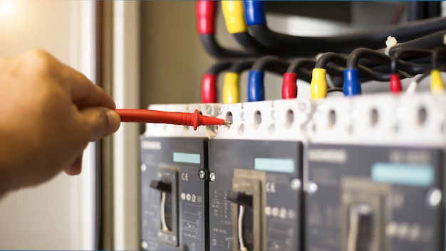 Testador de trabalho de engenheiro eletricista medindo tensão e corrente de linha elétrica de potência em controle de gabinete elétrico.