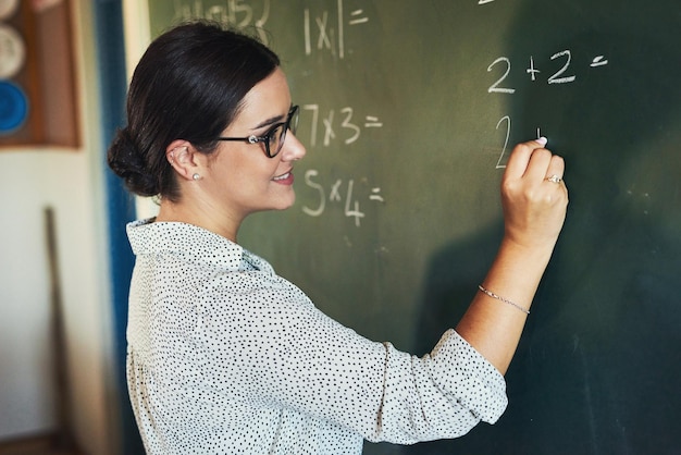 Testando meus alunos em suas habilidades matemáticas Foto de uma jovem e atraente professora sozinha e escrevendo no quadro-negro durante uma aula em sua sala de aula