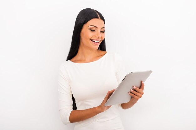 Testando seu novo brinquedo. Mulher jovem sorridente trabalhando em um tablet digital em pé contra um fundo branco