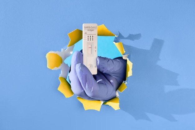 Teste covid rápido na mão na luva através do buraco de papel mão segurando um teste rápido de detecção de anticorpos