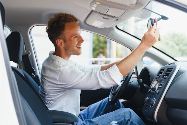 Teste de condução de veículo elétrico de nova geração com sistema de direção automática. Homem caucasiano bonito sentado ao volante do carro novo e moderno e sorrindo para a câmera.