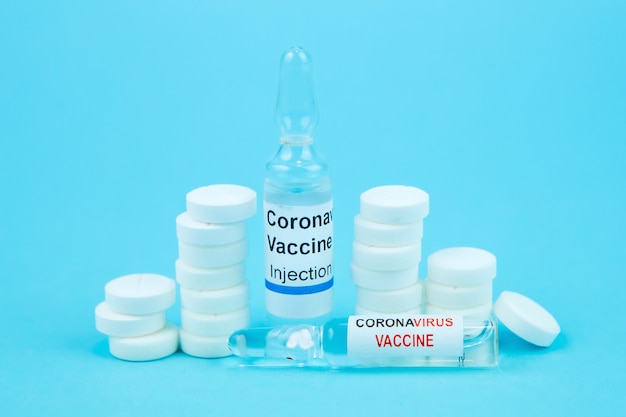 Teste de vacina contra coronavírus. frascos com medicamentos, pílulas, seringas, termômetro, máscara médica sobre uma mesa azul. uma cura para a gripe sazonal e o resfriado comum. meios para o tratamento da covid-19