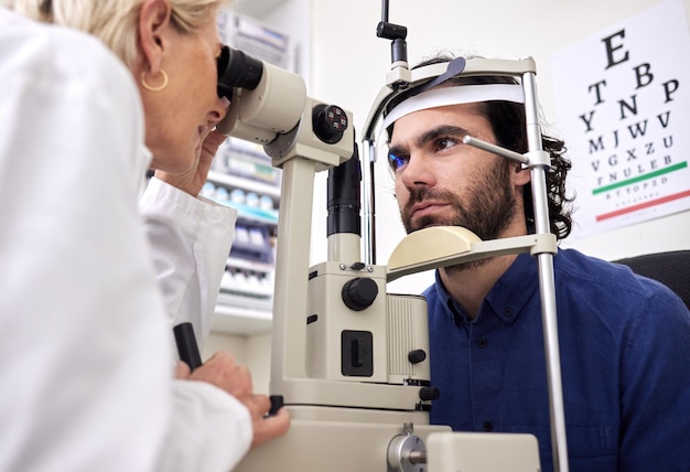 Teste de visão de exame oftalmológico e paciente com lente de laser e médico em consulta de optometria Rosto de um homem e uma pessoa de saúde com máquina para olhos, bem-estar e seguro de saúde com atendimento especializado