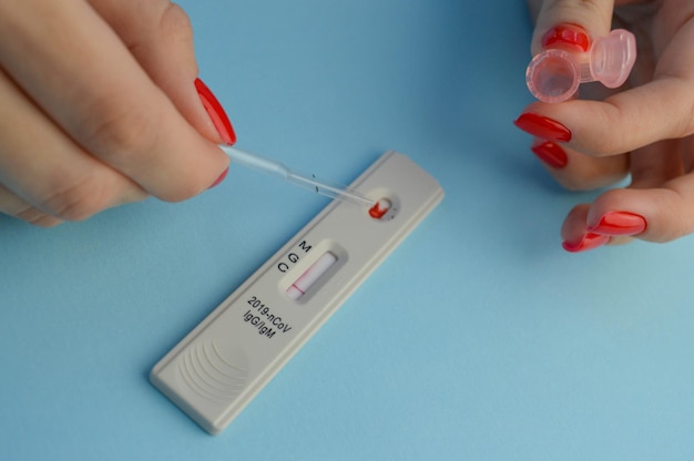 Teste para coronavírus em uma garota de fundo azul com uma manicure vermelha brilhante faz um exame de sangue