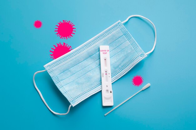 Teste rápido do Coronavirus e uma máscara médica no fundo azul com silhuetas rosa do Coronavirus