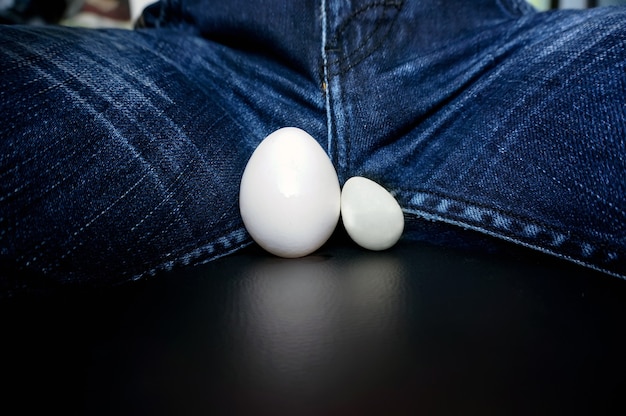 Los testículos masculinos, en forma de huevos de gallina, entre las piernas del chico de los jeans. Enfermedad de los órganos genitales masculinos. testículos inflamados agrandados. Cancer testicular