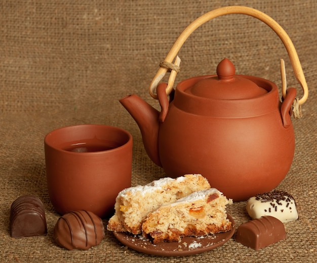 Tetera de barro con dulces, taza y pastel en el fondo del saco