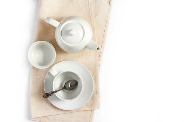 Tetera blanca y taza de té vacía con cuchara sobre tela beige aislado sobre fondo blanco endecha plana