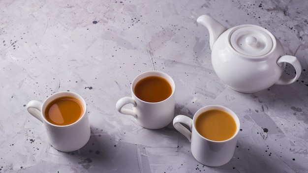 Tetera blanca y tazas blancas de té o café en una mesa gris