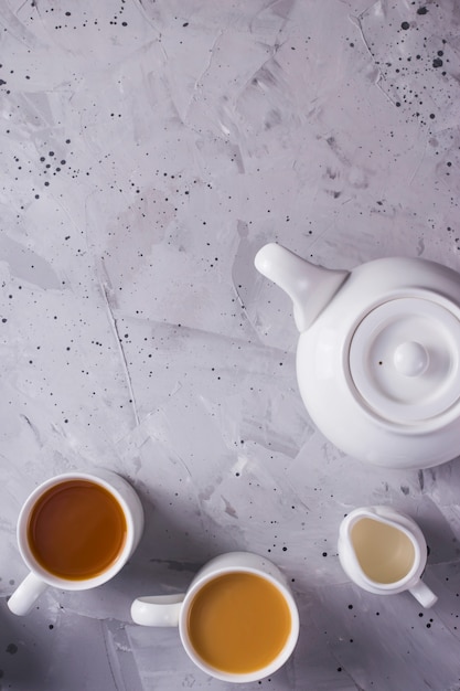 Tetera blanca y tazas blancas de té o café en una mesa gris