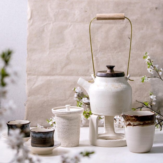 Tetera de cerámica blanca y negra hecha a mano con tazas de cerámica negra jarra katakuchi y cerezo floreciente como decoración de pie sobre una mesa de mármol Ceremonia tradicional japonesa del té Imagen cuadrada