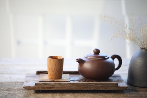 Tetera de cerámica y taza de té de bambú en bandeja de madera