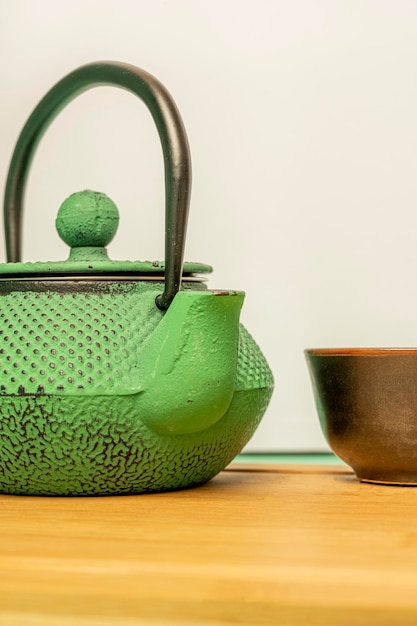 Foto tetera de hierro fundido verde de estilo asiático tradicional sobre una mesa de bambú y con una pequeña taza de té negro al lado