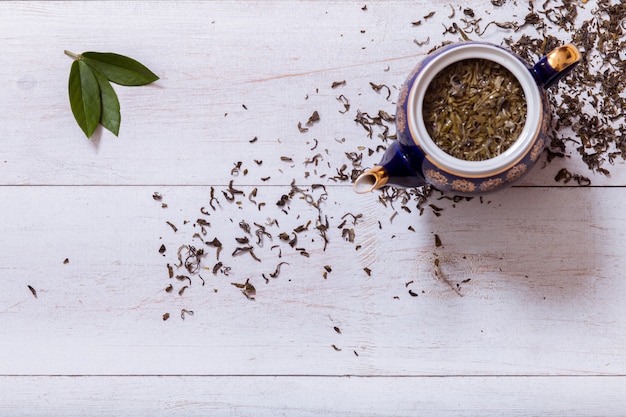 Tetera y hojas de té secas sobre fondo de madera blanca, vista superior, espacio de copia