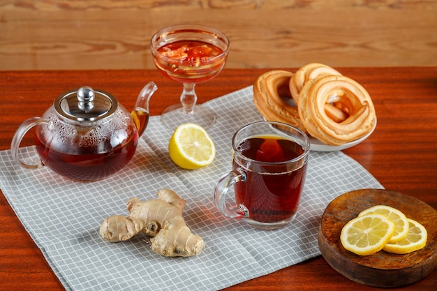 Una tetera de infusión de té fuerte en una servilleta junto a limón, jengibre y mermelada y donas